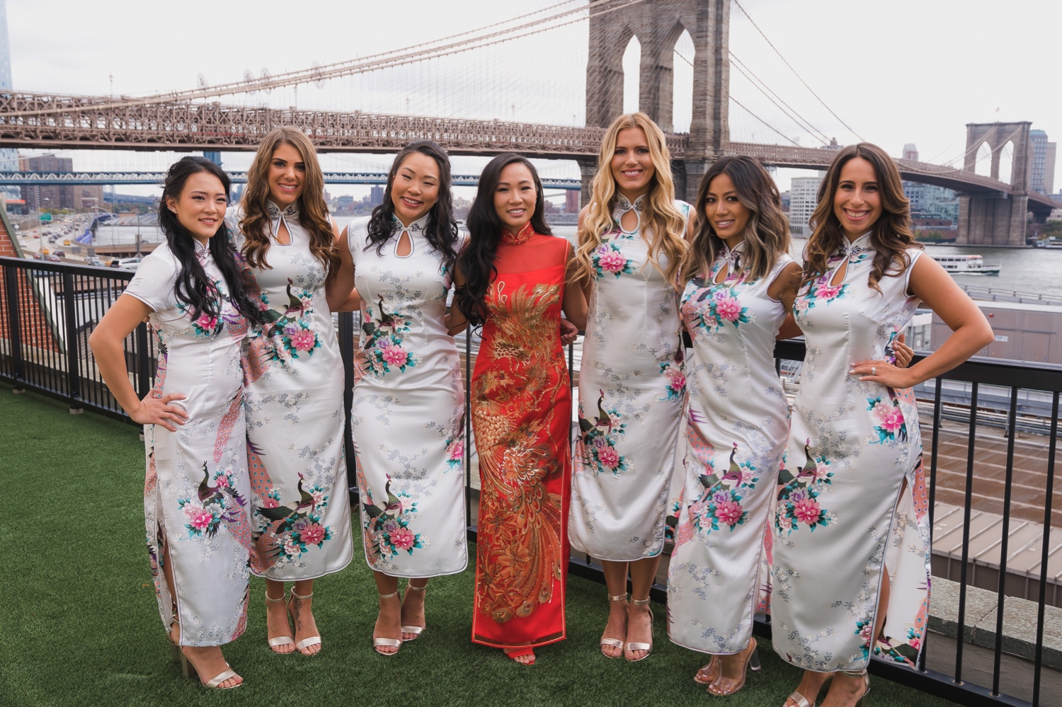 A bride and bridesmaids wearing a chinese dresses with a view of brooklyn bridge in Mr. C Seaport Hotel before Cipriani Wedding in New York City.