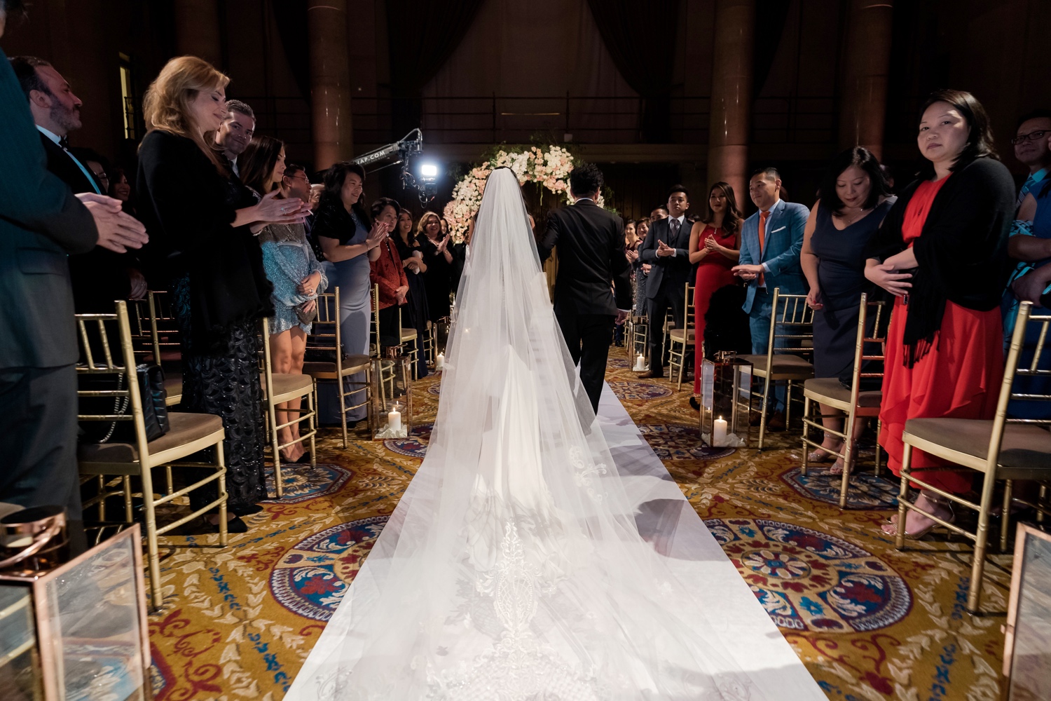 A bride and her father walking in an aisle during a wedding ceremony at Cipriani Wall Street in New York City. Wedding Dress by Pronovias