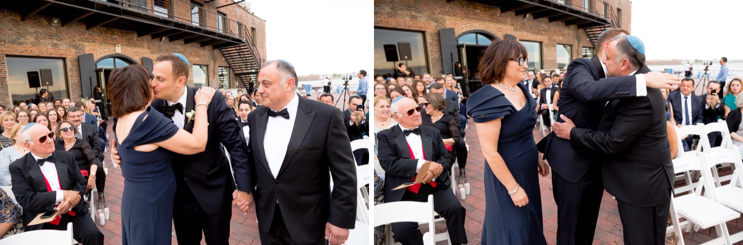 A groom and his parents walking and hugging in an aisle during a wedding ceremony at Liberty Warehouse, Brooklyn New York. 