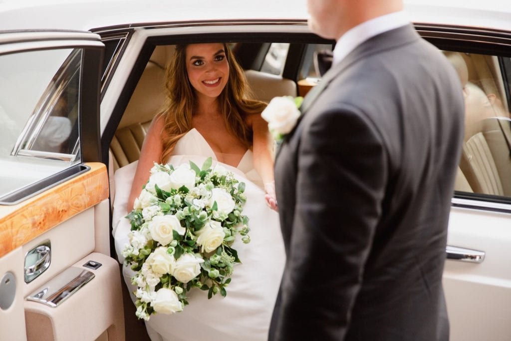 A newly wedded bride getting out a limo while holding her husband's hand.