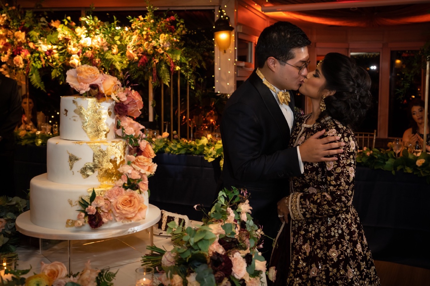 A newly wedded couple kissing next to their wedding cake during a wedding reception at the Tappan Hill Mansion.