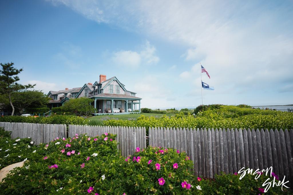 Shingled seaside house behind a weathered wooden fence and beach roses on Nantucket