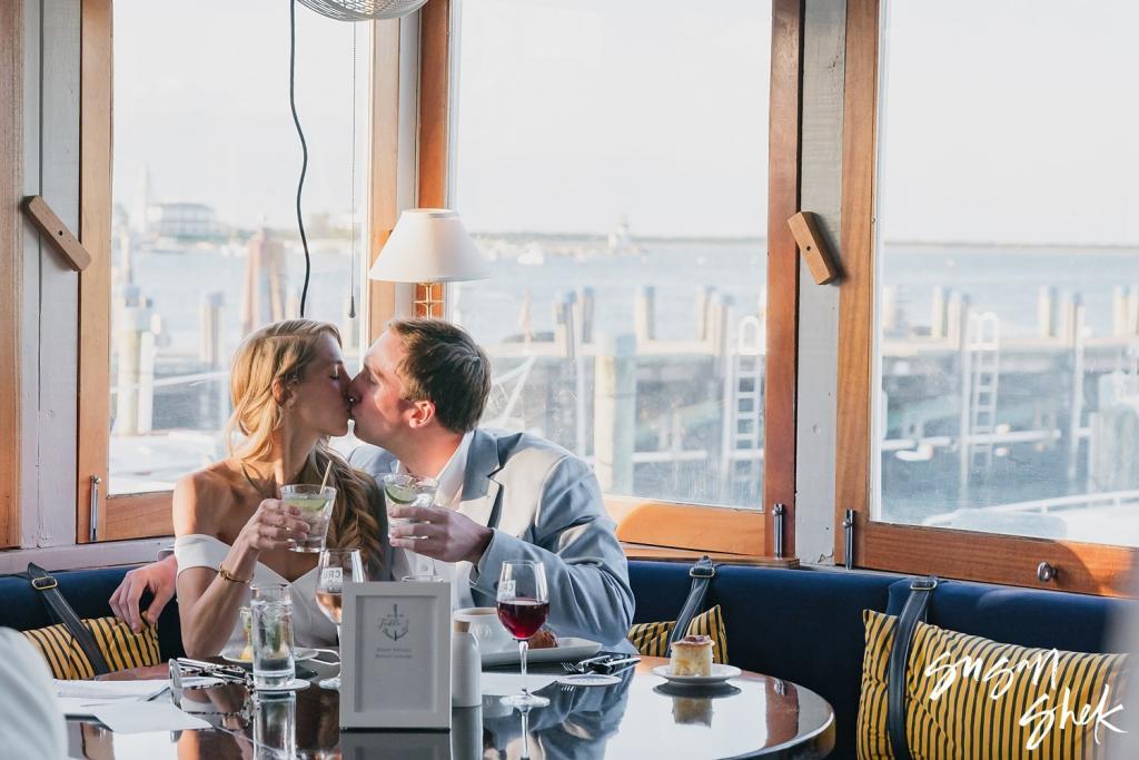 Couple kissing at a window table overlooking the harbor