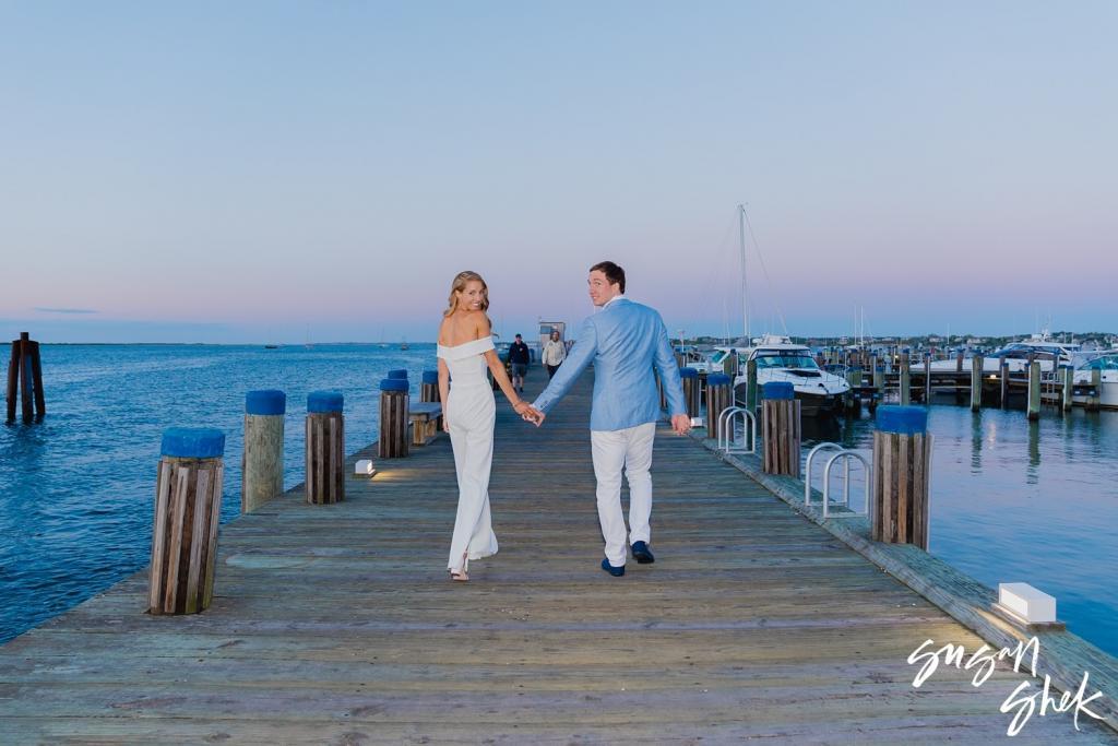 Couple walking hand in hand down a wooden pier at dusk in Nantucket harbor