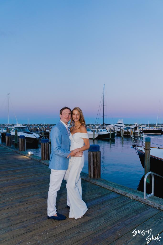 Couple standing close on the pier with boats in the marina behind them