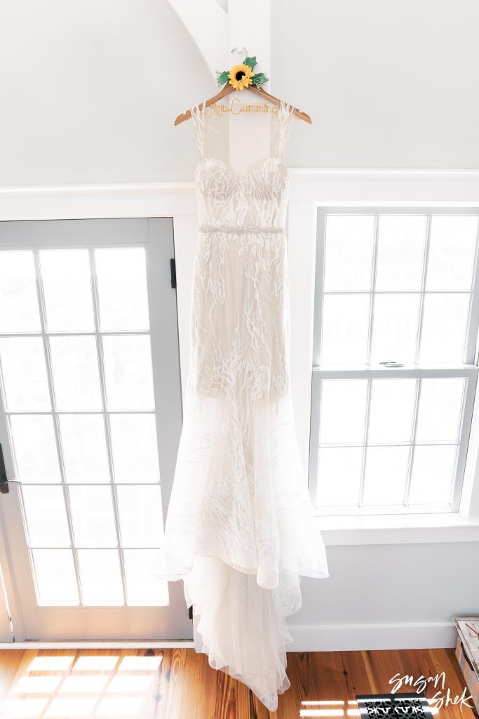 Lace wedding gown hanging in a bright window, a sunflower tied to the hanger