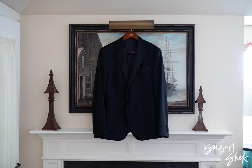 Groom's tuxedo jacket hanging over a fireplace below a painting of a sailing ship