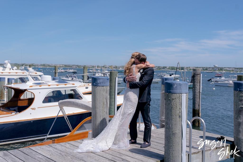 Bride and groom embracing on the dock beside wooden boats in Nantucket harbor