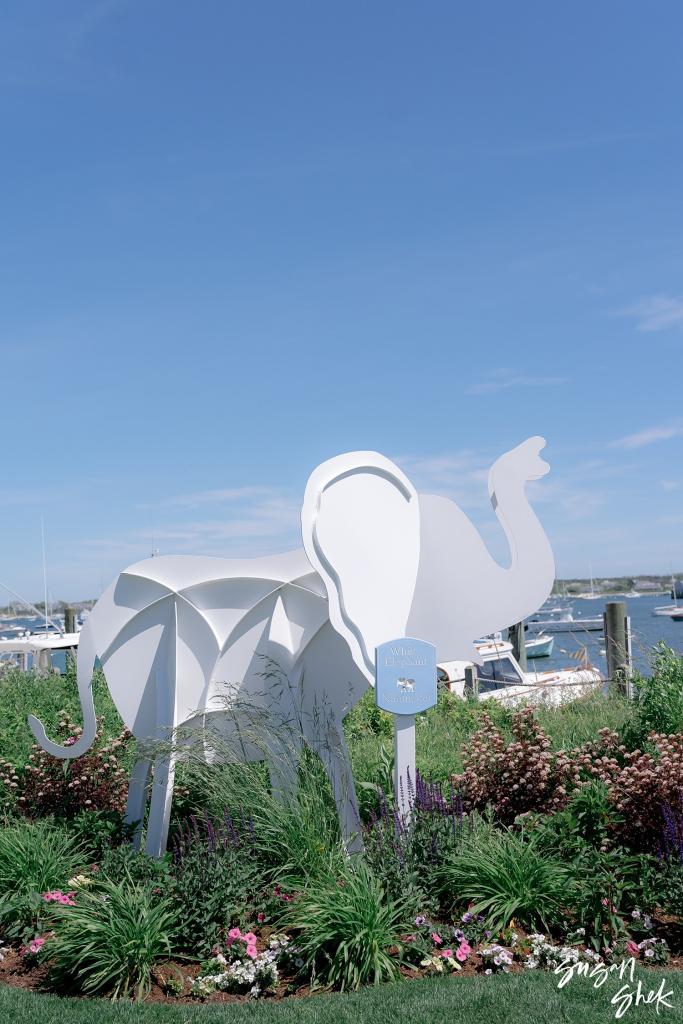 White sculpted elephant standing in a flower garden by the harbor
