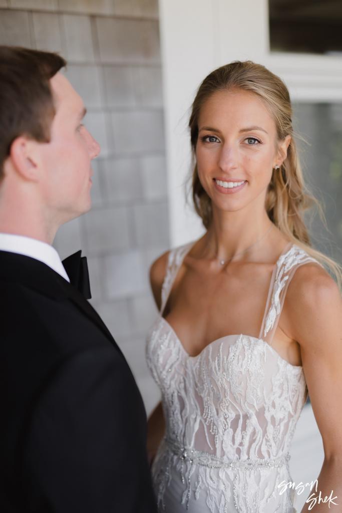 Bride smiling beside the groom against a shingled wall