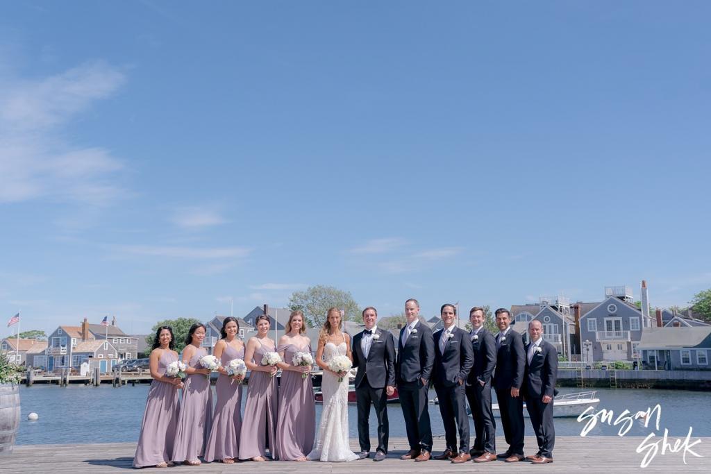 Full wedding party lined up along the harbor under a wide blue sky