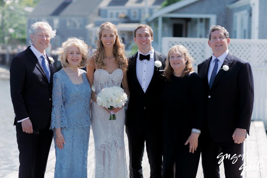 Bride and groom with family on the dock in front of shingled houses