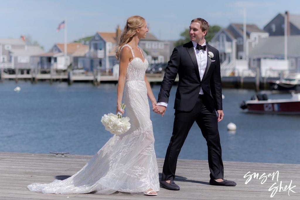 Bride and groom laughing as they walk along the dock with her bouquet in hand