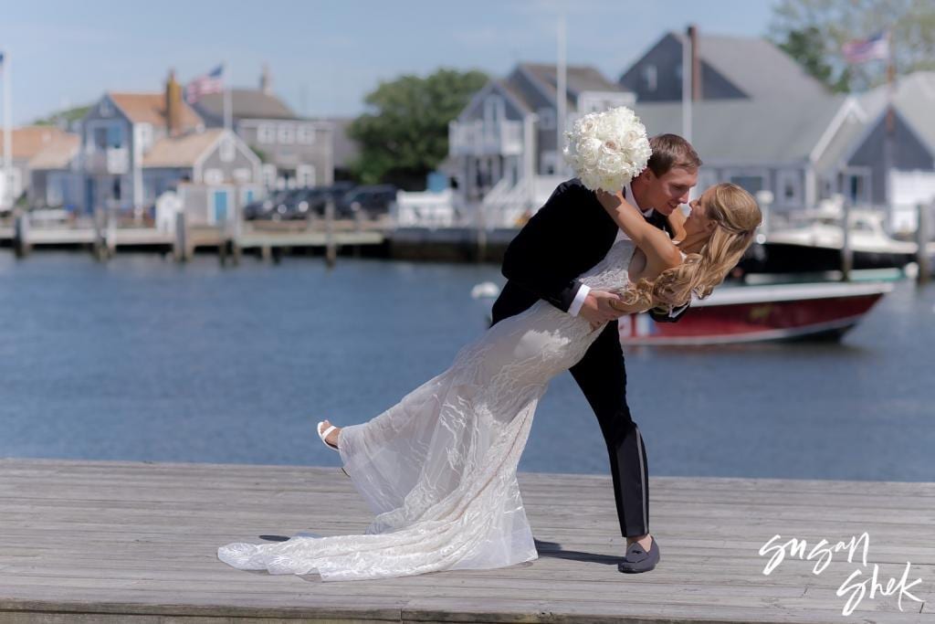 Groom dipping the bride into a kiss on the dock, bouquet raised high