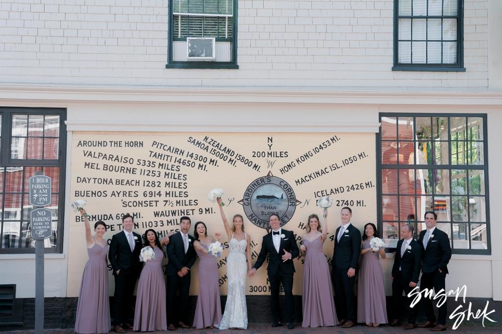 Wedding party cheering beneath a painted sign listing distances from Nantucket to ports around the world