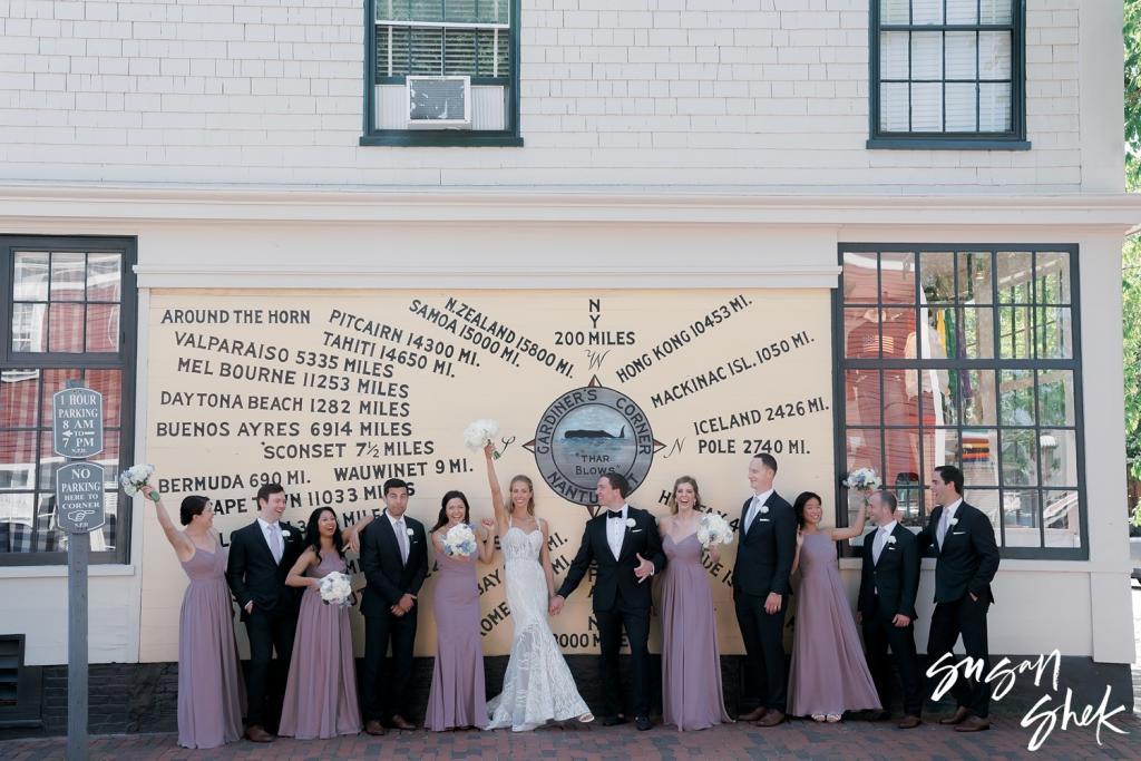 Wedding party posing beneath a painted sign listing distances from Nantucket to places around the world