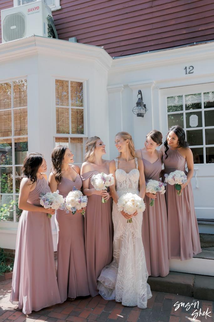 Bride and bridesmaids in mauve dresses outside a white storefront