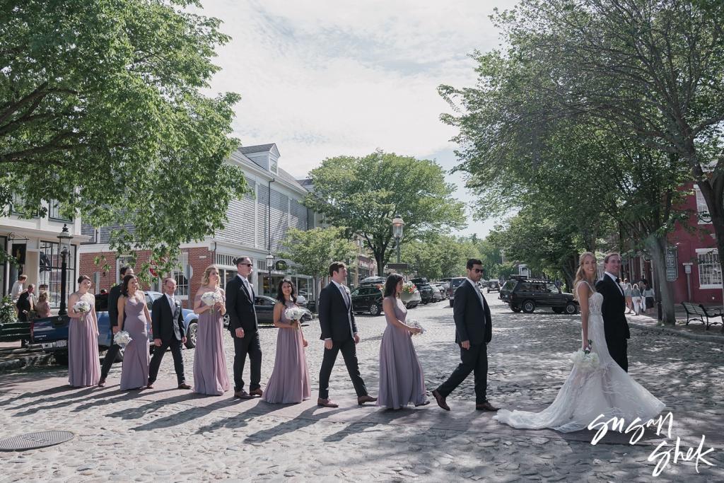 Wedding party walking in a line down a tree lined cobblestone street