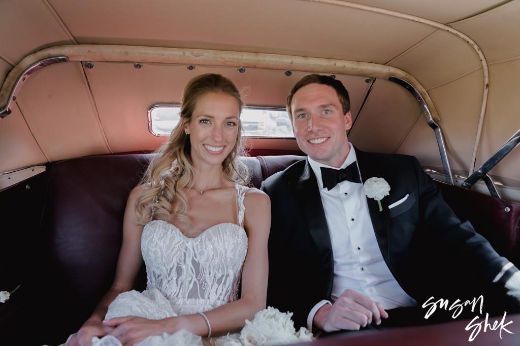 Bride and groom smiling in the back seat of a vintage convertible