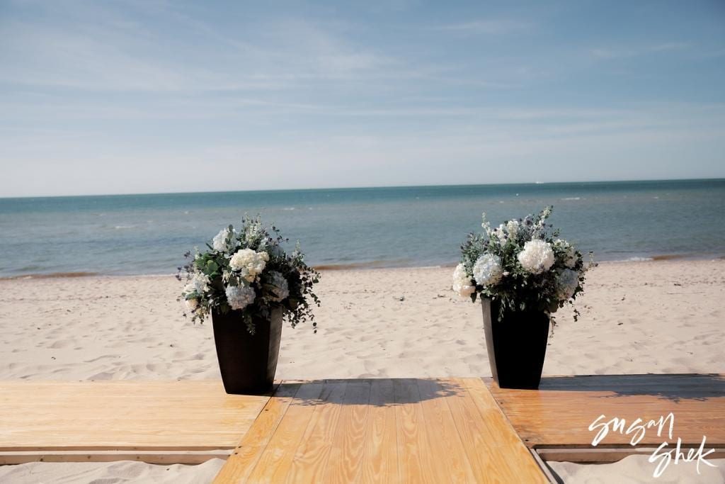 White flower arrangements at the end of a wooden aisle on the beach