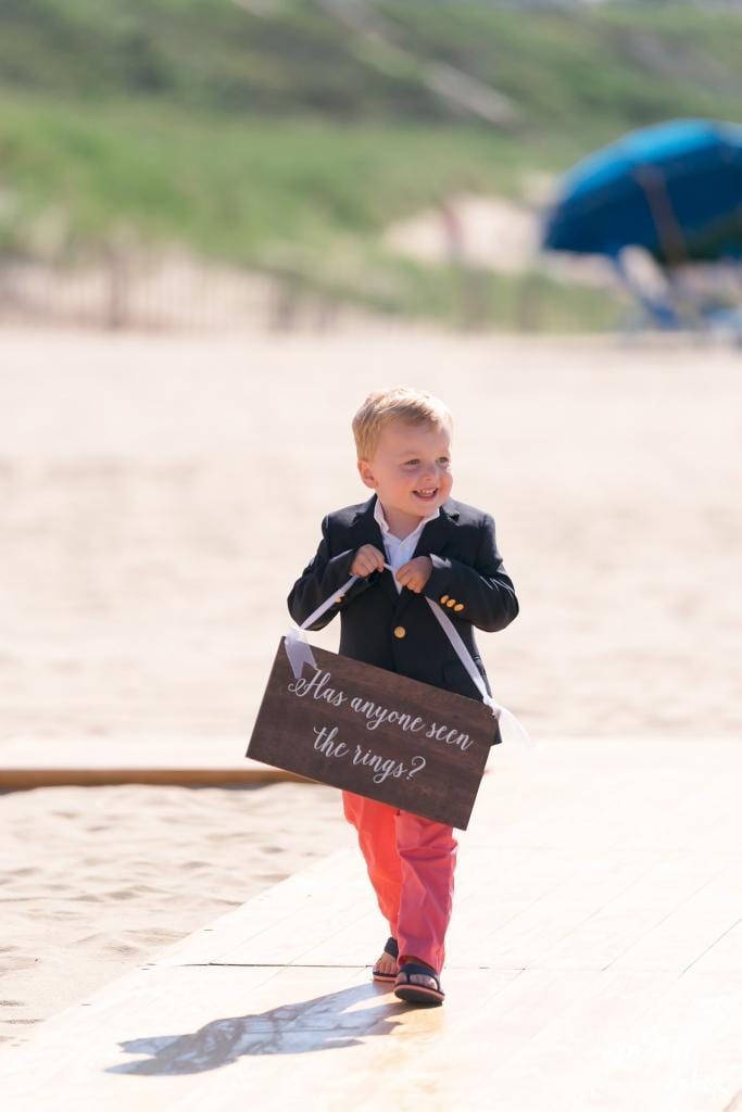 Ring bearer in red pants carrying a sign down the beach aisle