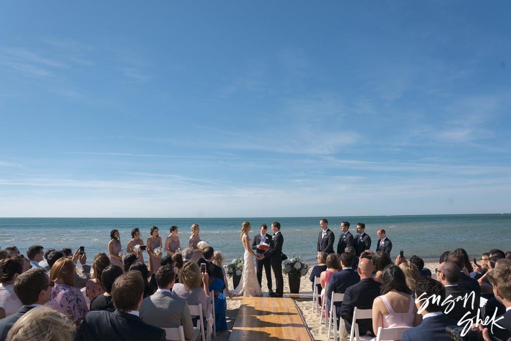 Wedding ceremony on Galley Beach facing the ocean, with guests seated on both sides of the aisle