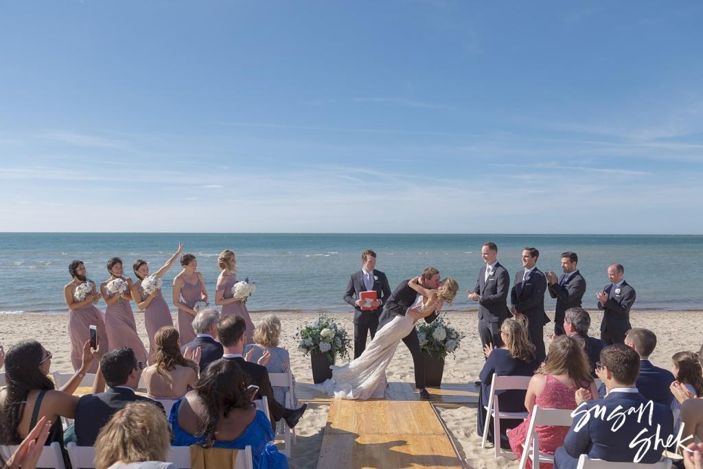 Bride and groom kissing at the end of the beach ceremony as guests cheer