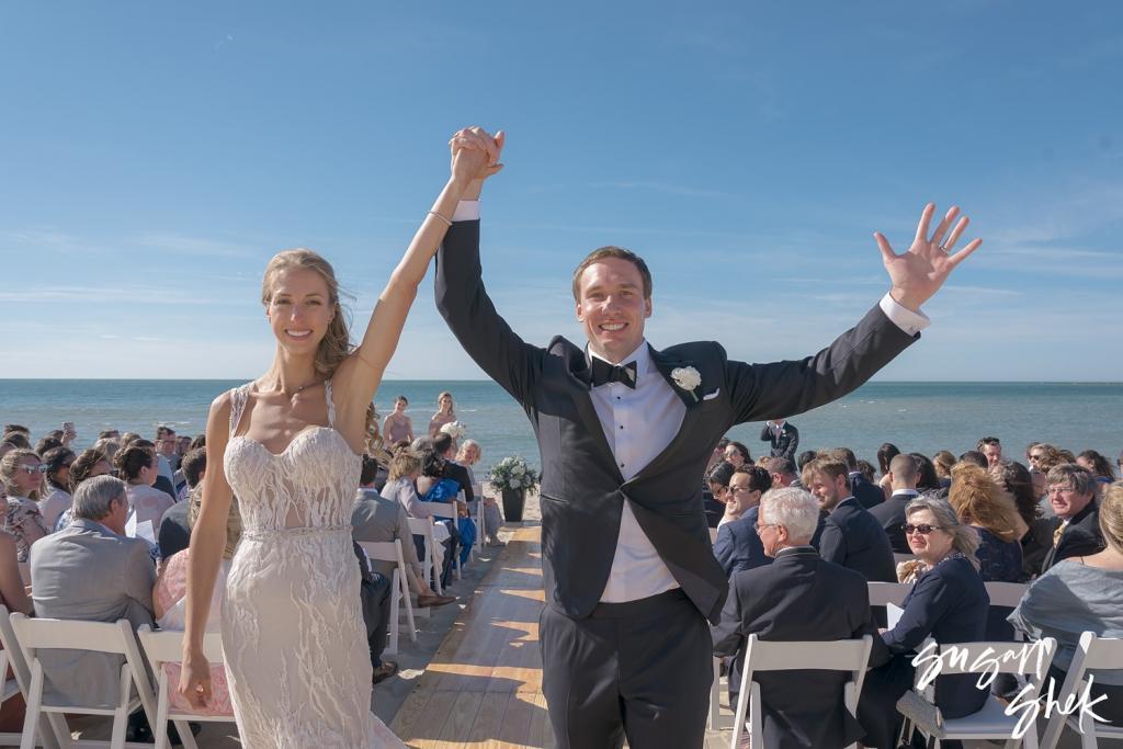 Newlyweds raising their arms as they walk back up the aisle after their beach ceremony
