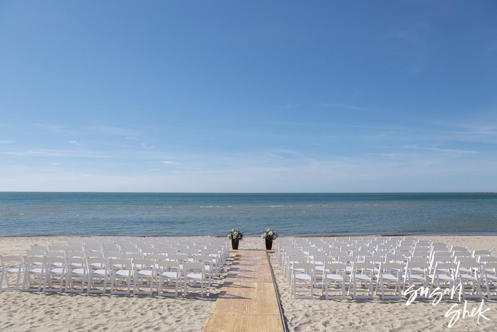 Empty white chairs lined up on the sand on either side of the aisle before the ceremony