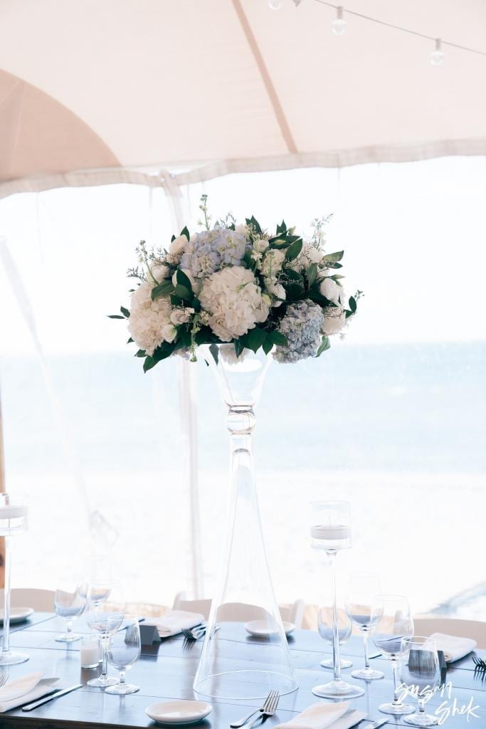 Tall white floral centerpiece above a reception table with the ocean behind