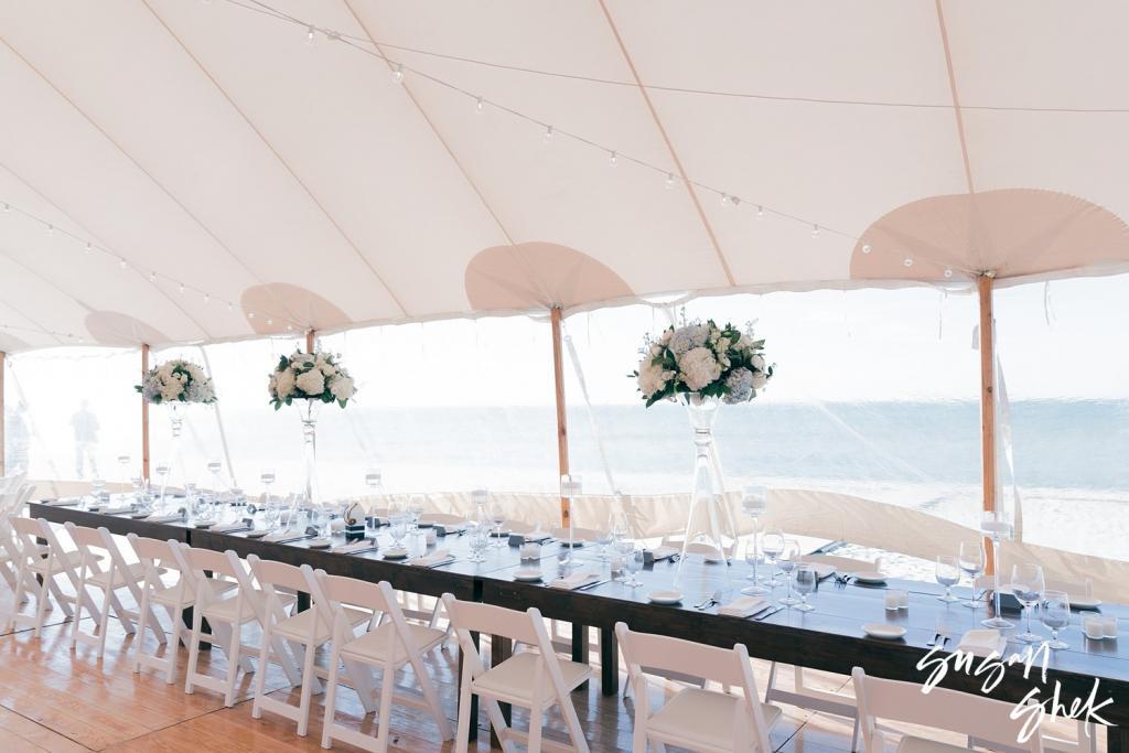 Long reception tables with white flowers under a sailcloth tent looking out to the ocean