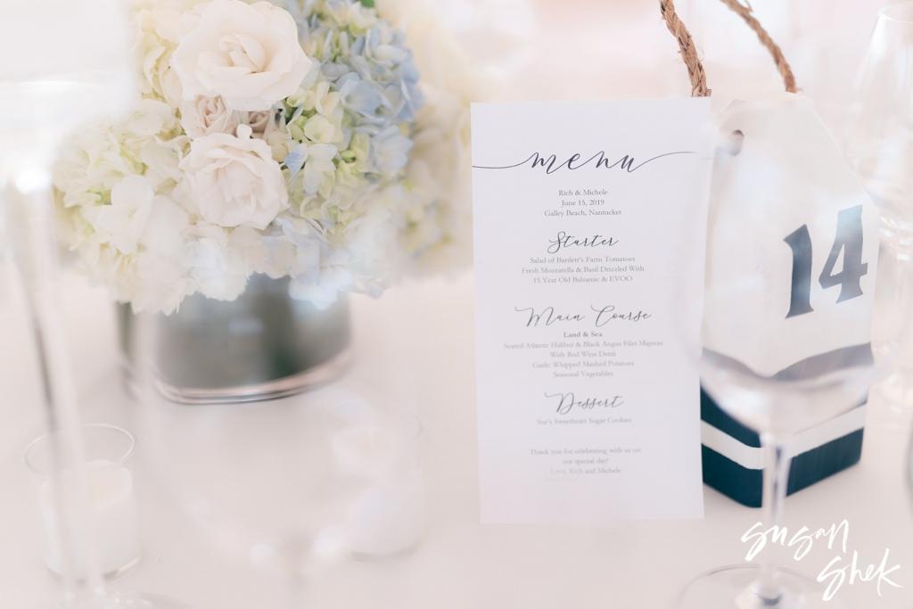 Calligraphy dinner menu beside white and blue hydrangeas and a buoy table number