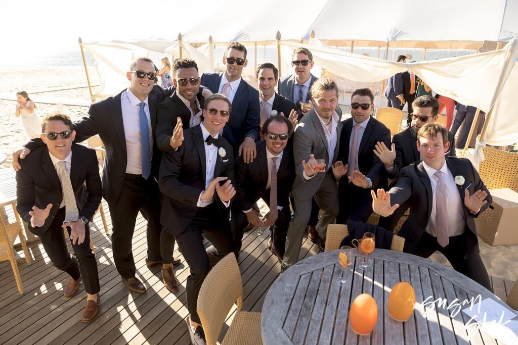 Groom and a group of friends in suits and sunglasses cheering on the deck