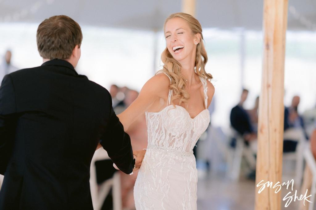 Bride laughing as she reaches for the groom's hands on the dance floor