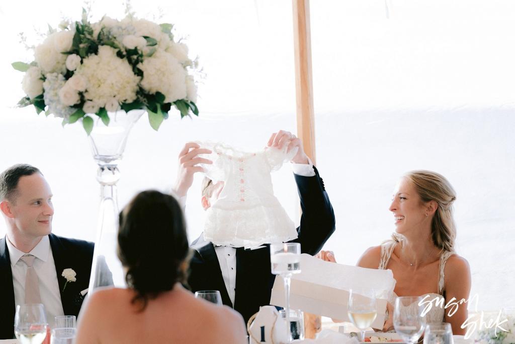 Guest holding up a baby outfit at the head table as the bride laughs