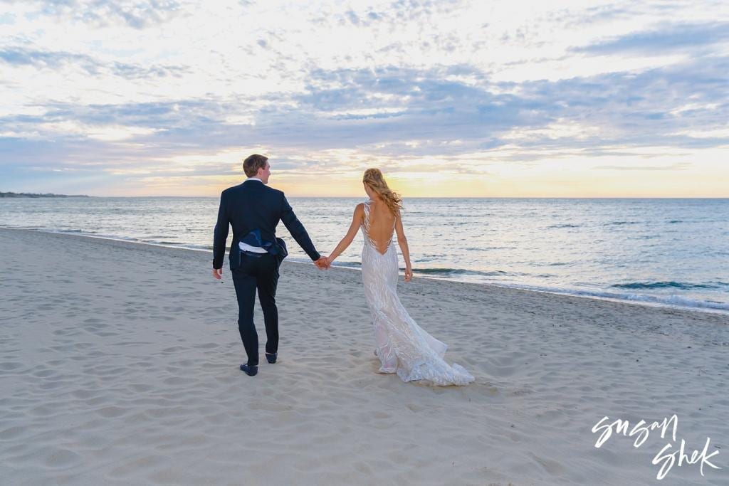 Bride and groom walking hand in hand along the shoreline at sunset