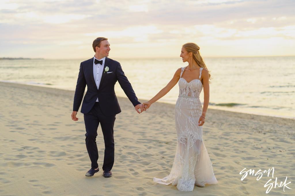 Bride and groom holding hands on the beach in golden evening light