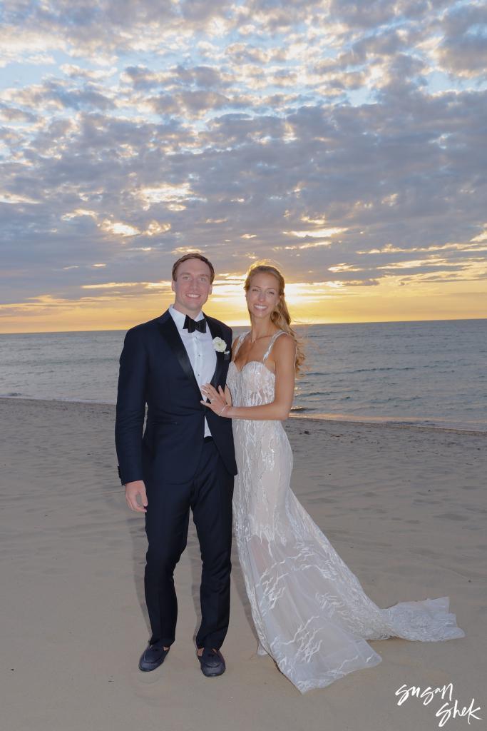 Bride and groom posing on the sand under a cloudy sunset sky