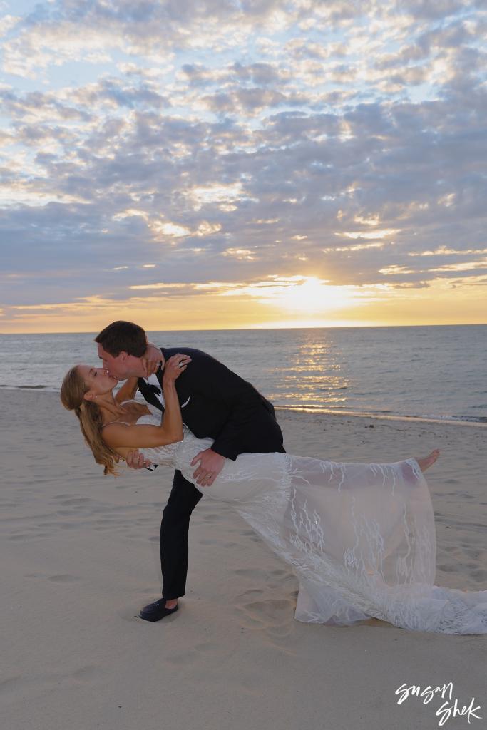 Groom dipping the bride into a kiss on the beach at sunset