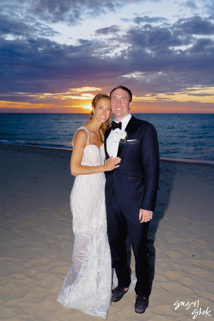 Bride and groom embracing on the beach as the sun sets