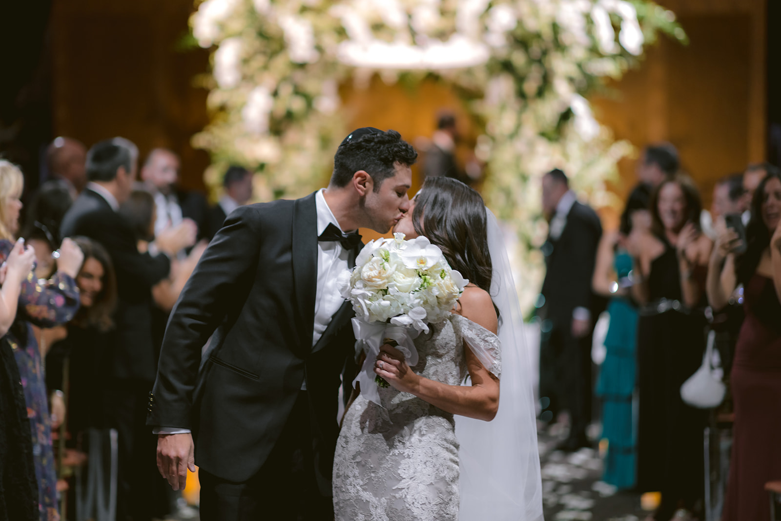 Bride and groom share a kiss during their wedding ceremony surrounded by guests
