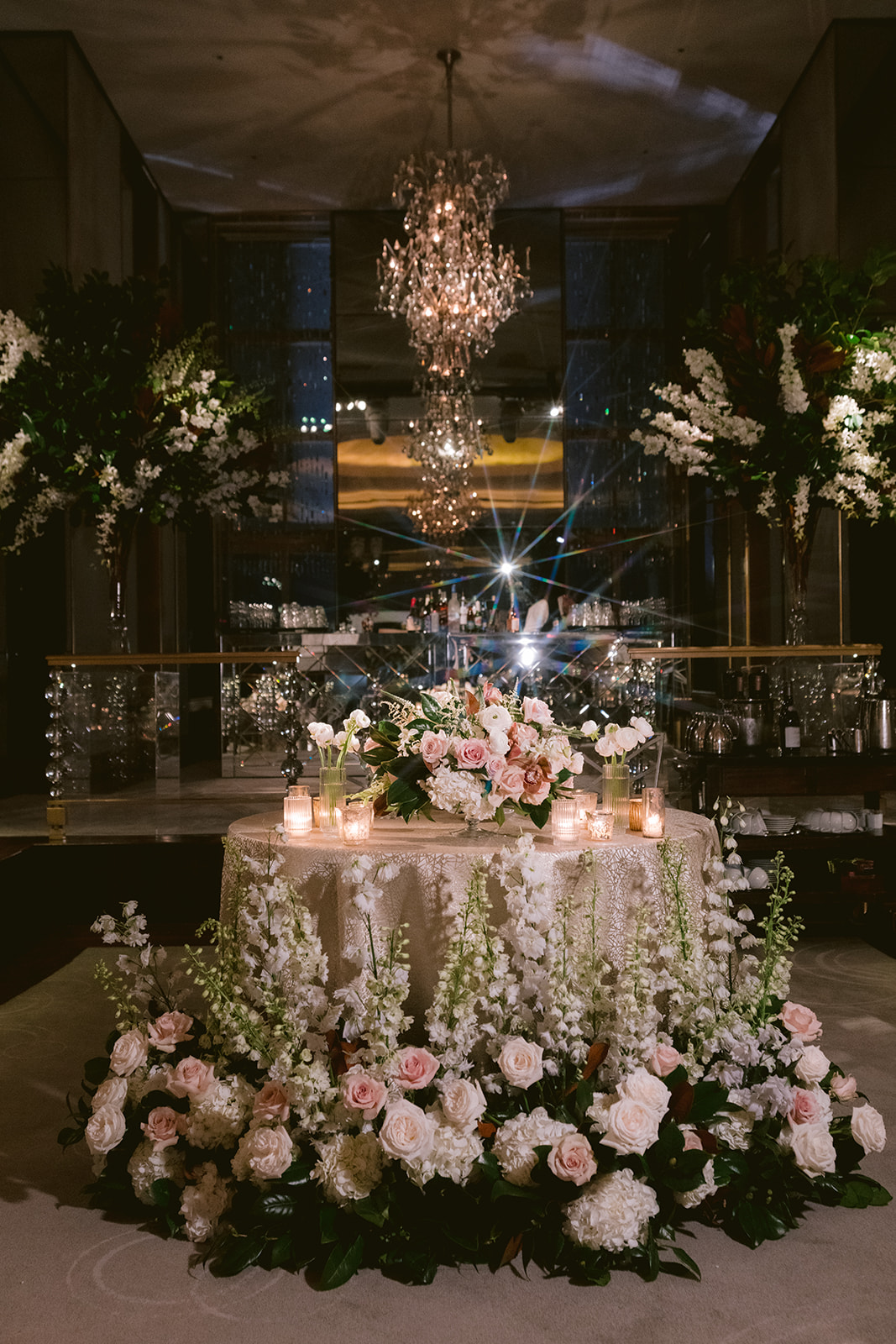 Romantic sweetheart table with blush and white floral arrangements, candles, and crystal chandeliers for an elegant wedding reception