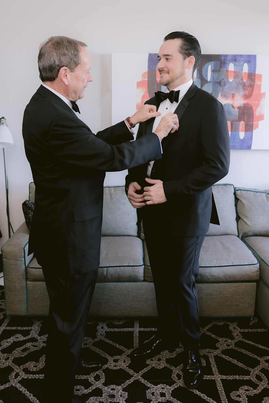 Father helping groom with bow tie during wedding getting ready photos
