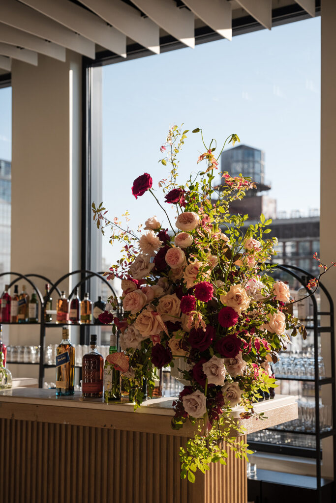 Floral arrangement at Vesper Events featuring deep red roses, blush blooms, and cascading greenery styled on the reception bar.