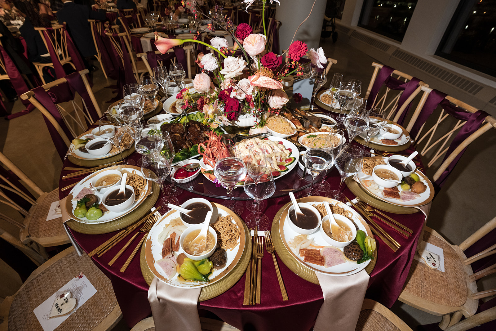 Traditional Chinese wedding banquet with lazy Susan centerpiece, multiple plated dishes, gold flatware, and burgundy linens.
