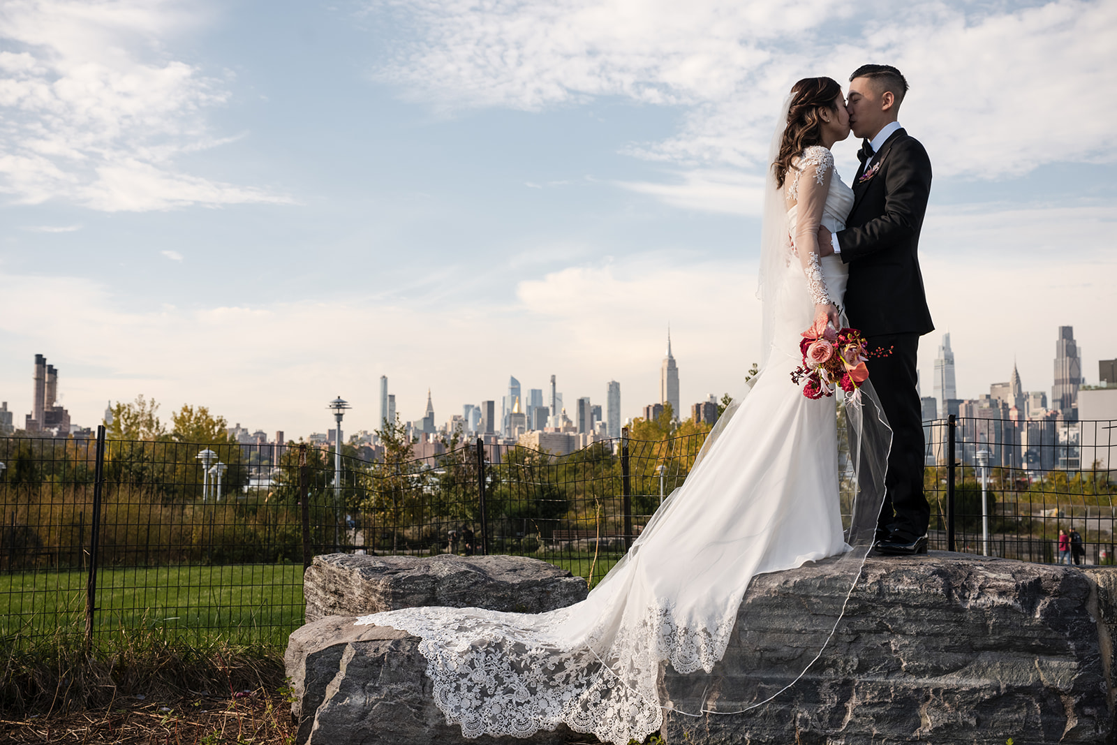 wide view photo of a bride and groom kissing on a rock at the vesper nyc wedding venue Vesper events park