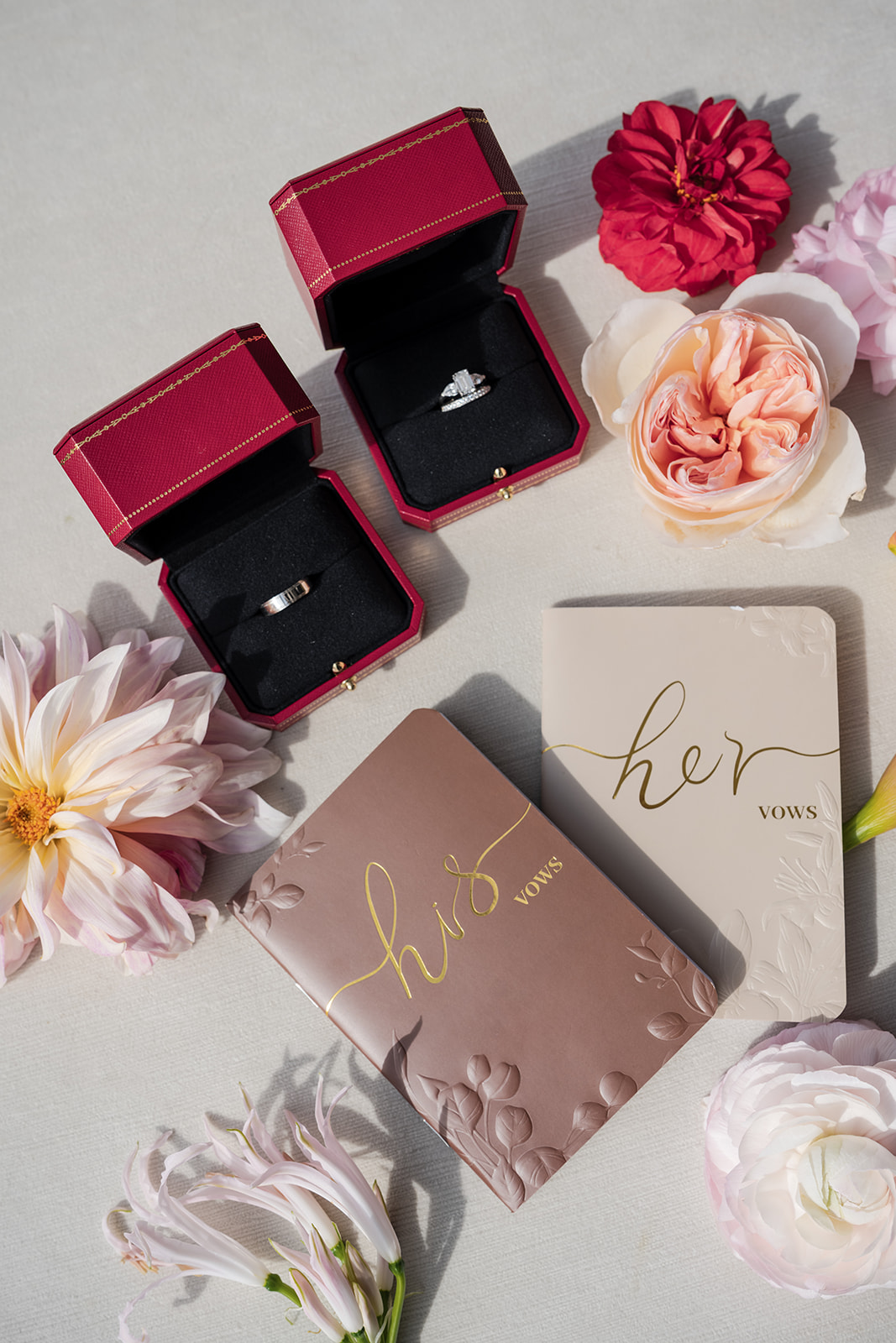 Wedding flat lay at Vesper Events featuring vow books, engagement ring, red velvet ring boxes, and romantic blush florals styled on neutral linen.