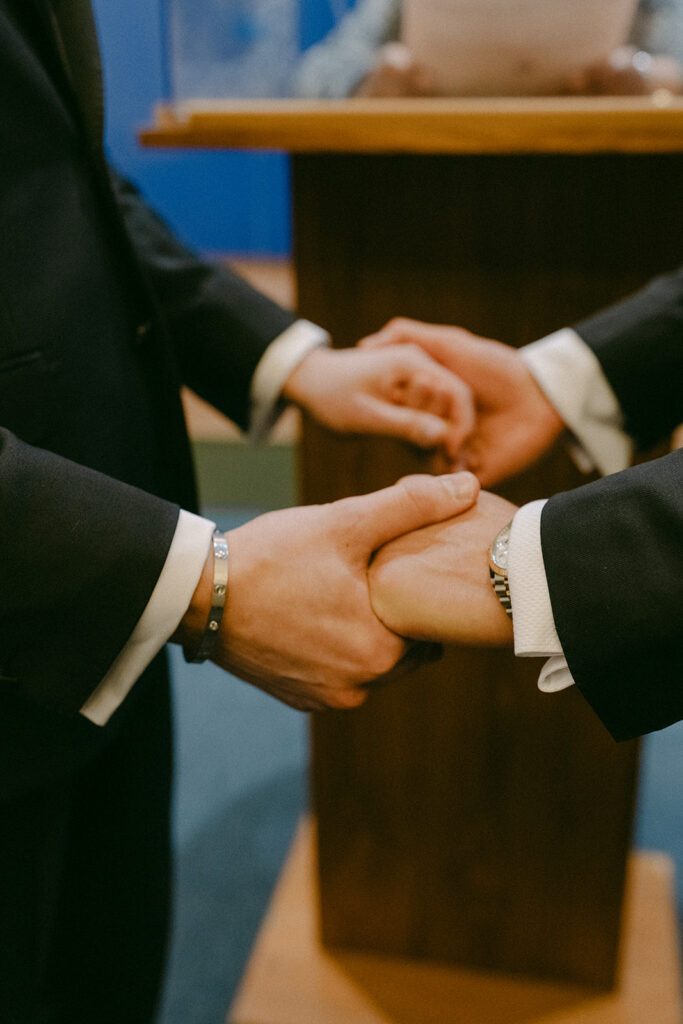 Two grooms holding hands at the officiant's podium during the ceremony