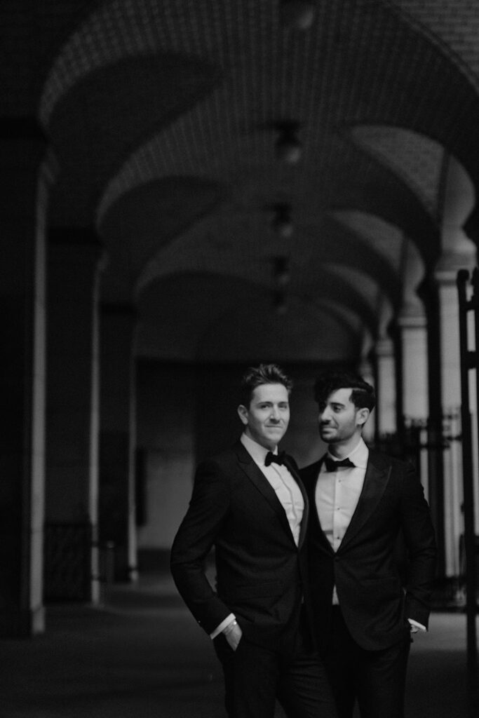 Black and white portrait of two grooms under a vaulted arcade