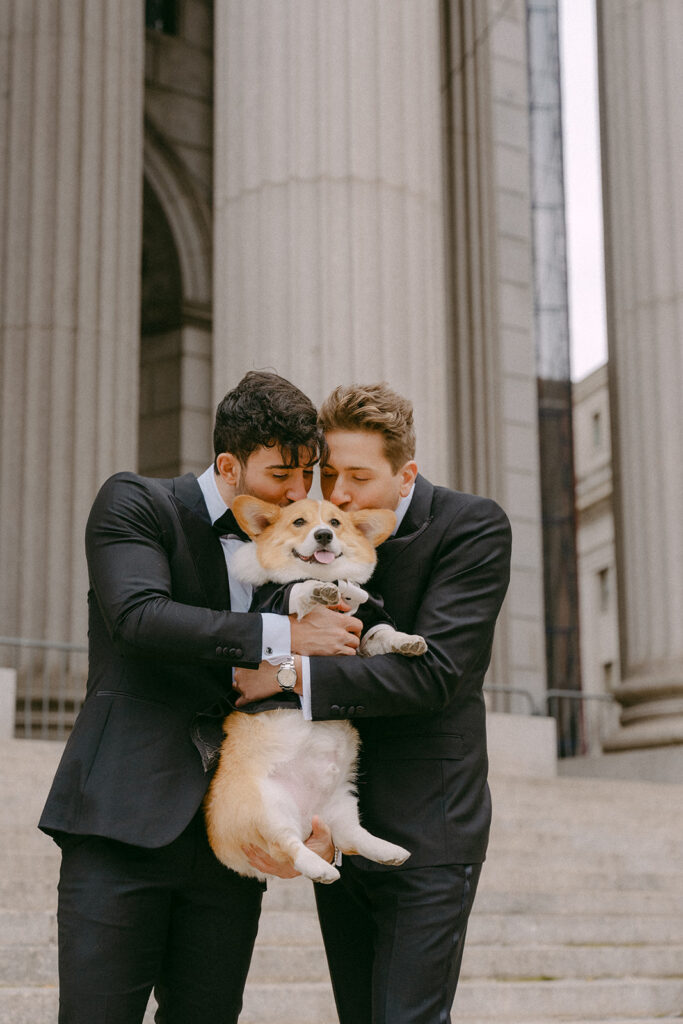 Two grooms holding their corgi between them on the courthouse steps